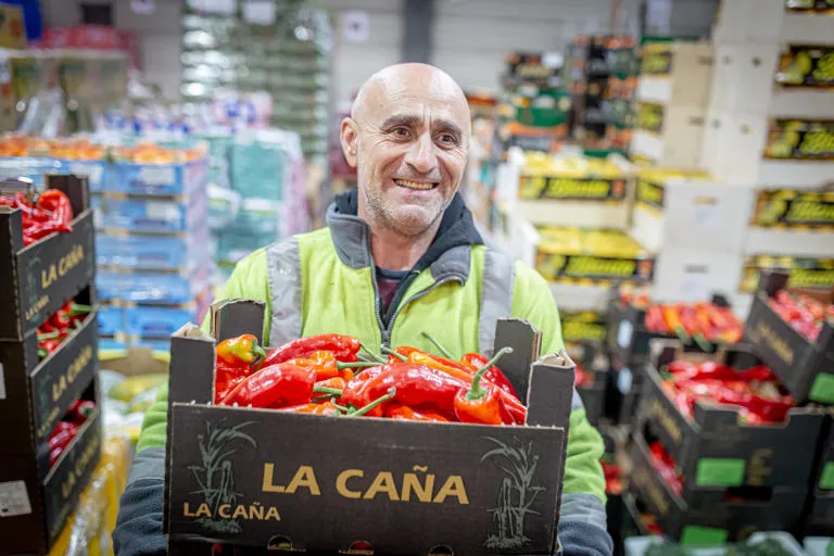market operative carrying carboard crate filled with peppers