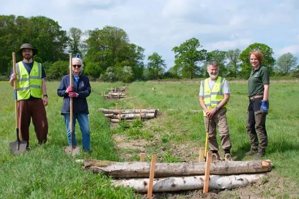 Four people stand on grass next to some logs, acting as leaky dams