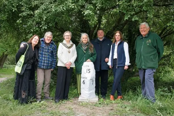 A group of men and women standing behind a white stone in front of a tree