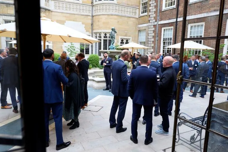 Attendees networking in a stone courtyard, with parasols, a central fountain statue, and historic buildings surrounding the space