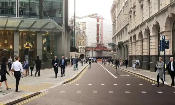 A wide London street scene showing proposed improvements, including a dedicated cycle lane in the centre, widened pavements with pedestrians walking, and modern office buildings alongside older architecture. Construction scaffolding is visible in the distance.