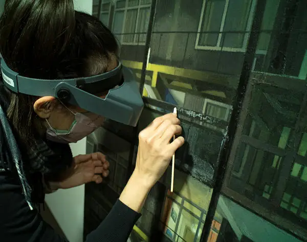Lady with glasses and mask cleaning a painting with a long cotton bud