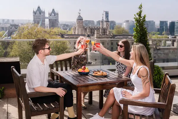 group of friends holding glasses in a rooftop bar with Tower Bridge and Tower of London in the background