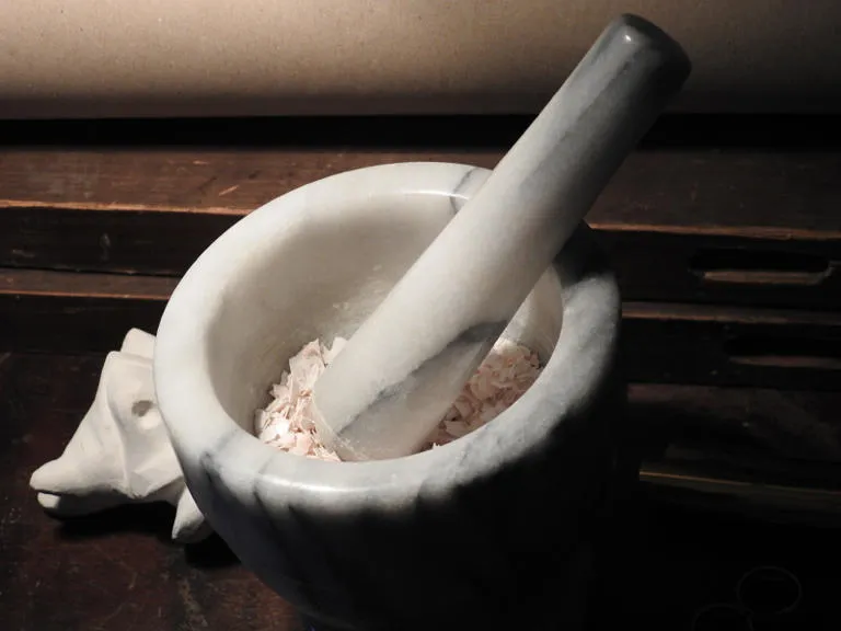 A white stone mortar and pestle being used to crush eggshells