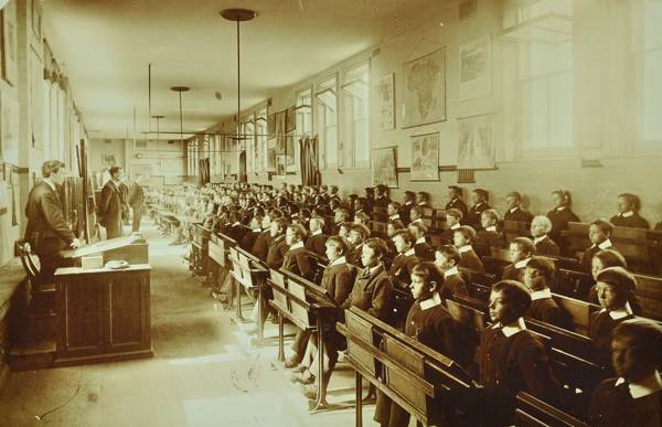 School boys sitting at desks, with four teachers, in a classroom at Ashford Residential School, c.1905