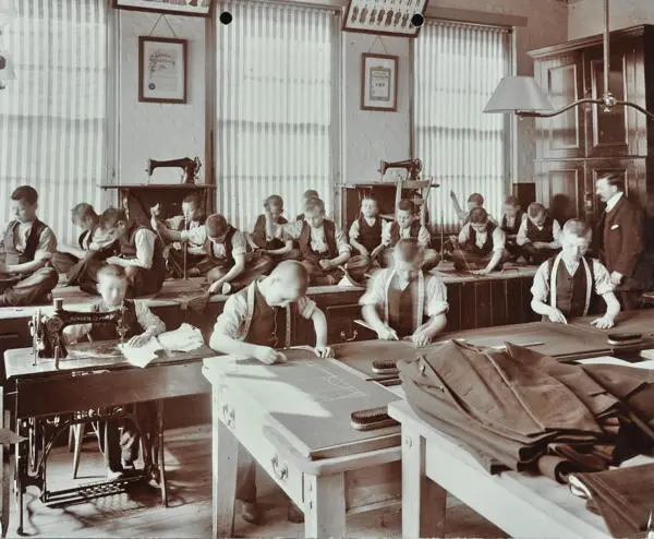 Boys sewing and drawing clothing patterns on tables at Highbury Industrial School in 1908