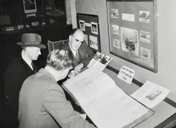 Three men looking at a LCC Fire Department log book being consulted in the Record Room at County Hall, 1954