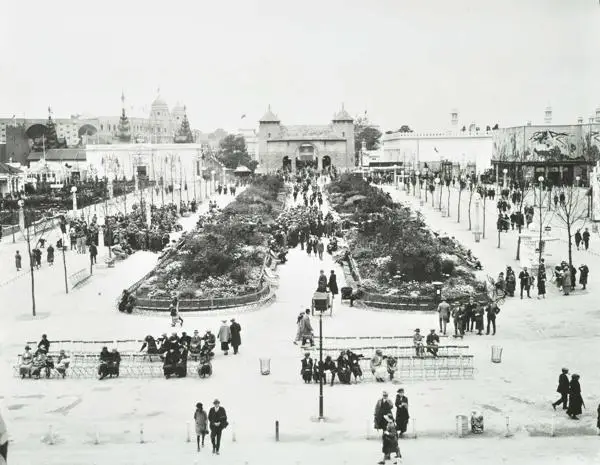 The British Empire Exhibition in 1924, with the stadium in the background. In the centre of the image, a crowded path leads to a replica of ‘Old London Bridge’