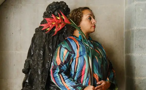 Sam facing away from Cass's statue, holding a red heliconia flower in front of his face