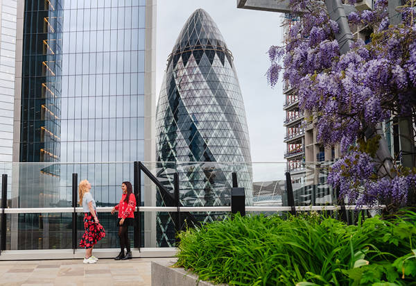 Two women chatting at a rooftop with views of the Gherkin